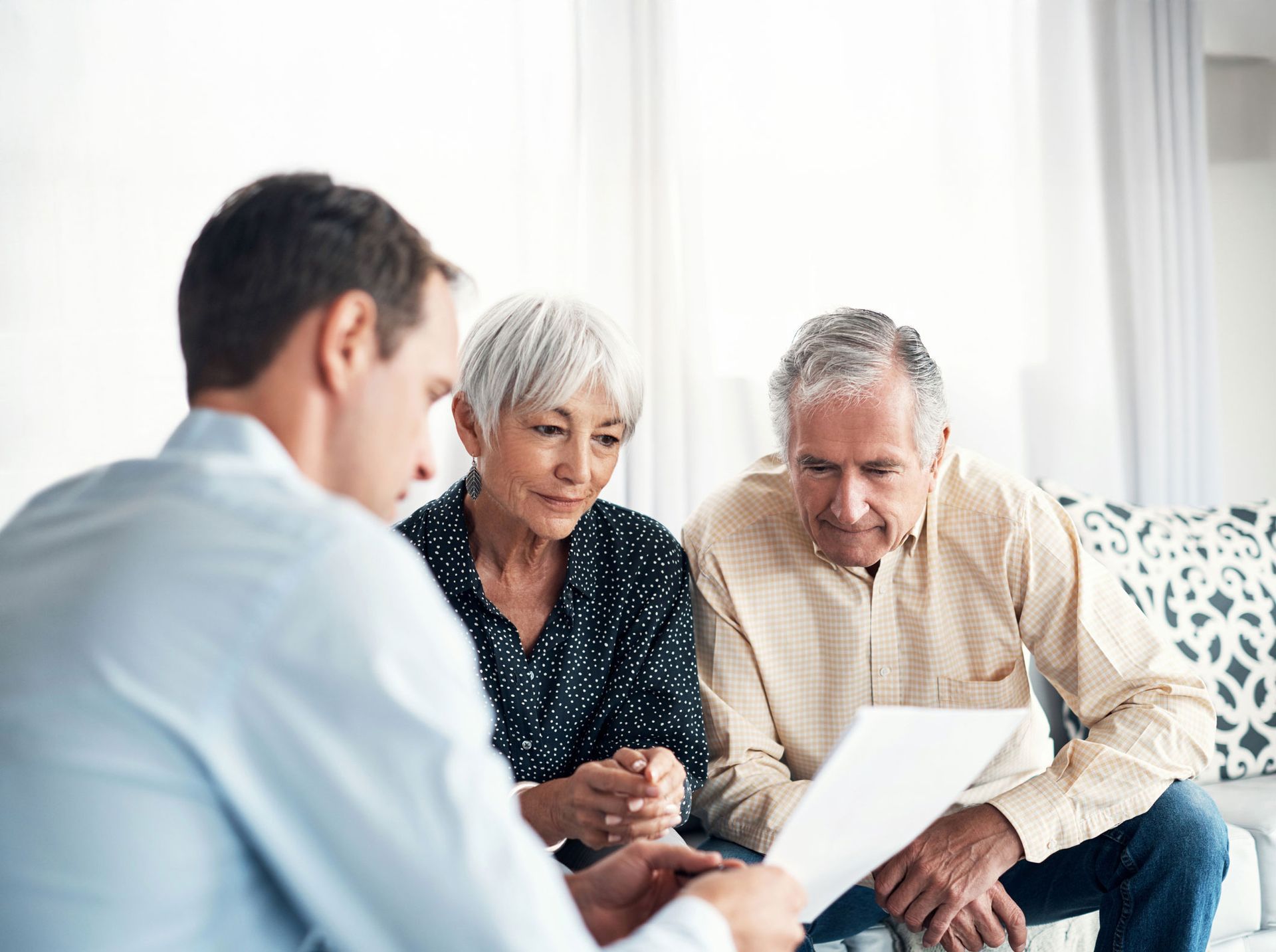 Financial advisor reviews paperwork with senior couple on a couch.